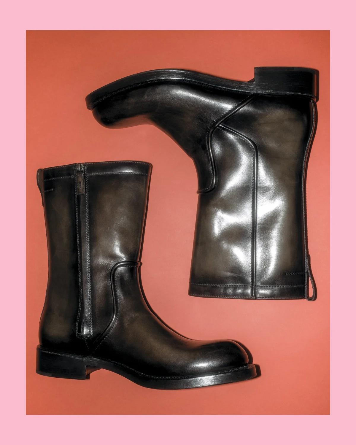 Stylish black knee-high leather boots displayed against a coral background.