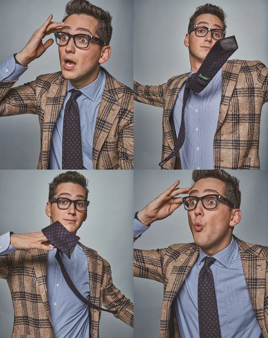 A man in a patterned blazer making playful facial expressions while adjusting his tie.