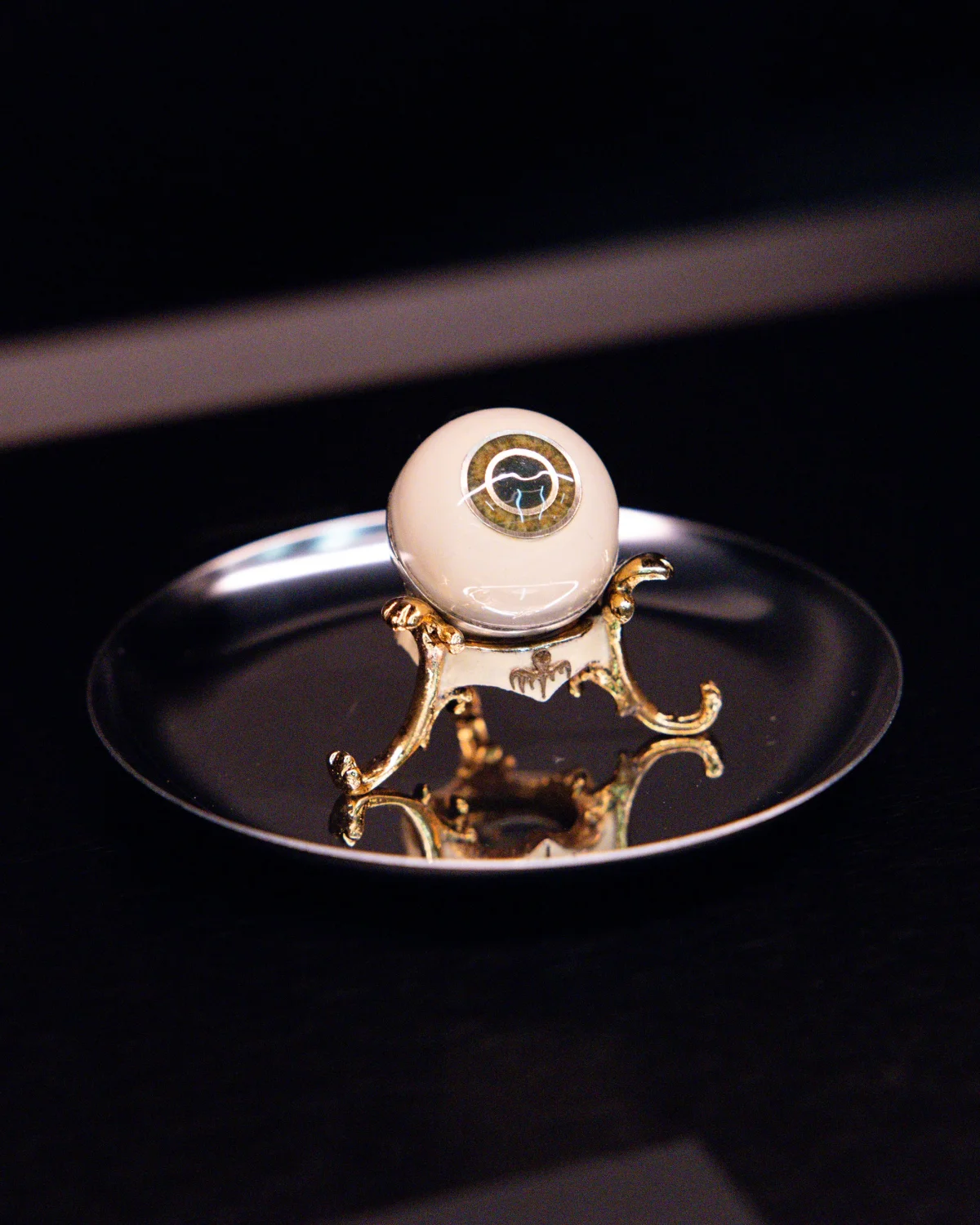A decorative artificial eye displayed on a gold stand in a reflective dish.